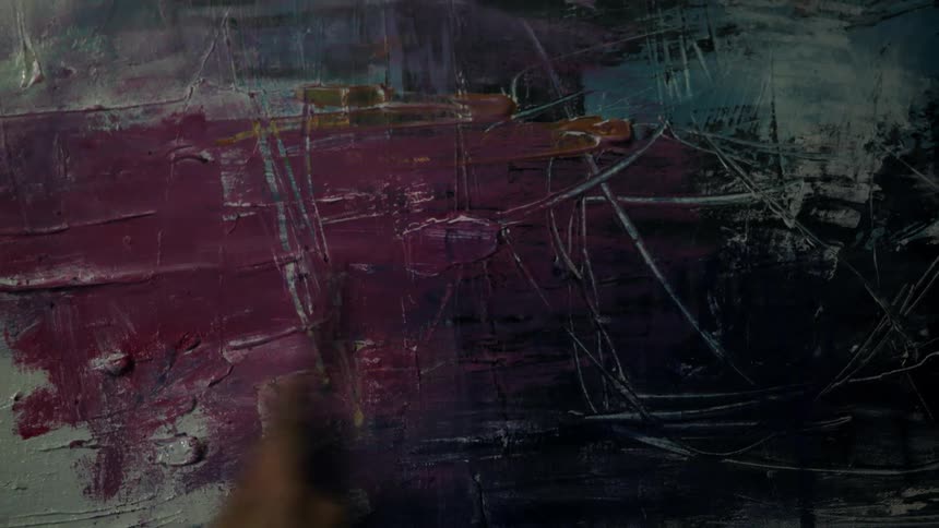A person scrapes the paint off a painted canvas using a palette knife