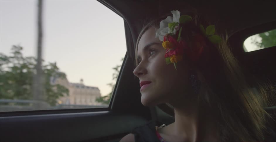 A woman with flowers in hair looks out of a window as she travels in a vehicle