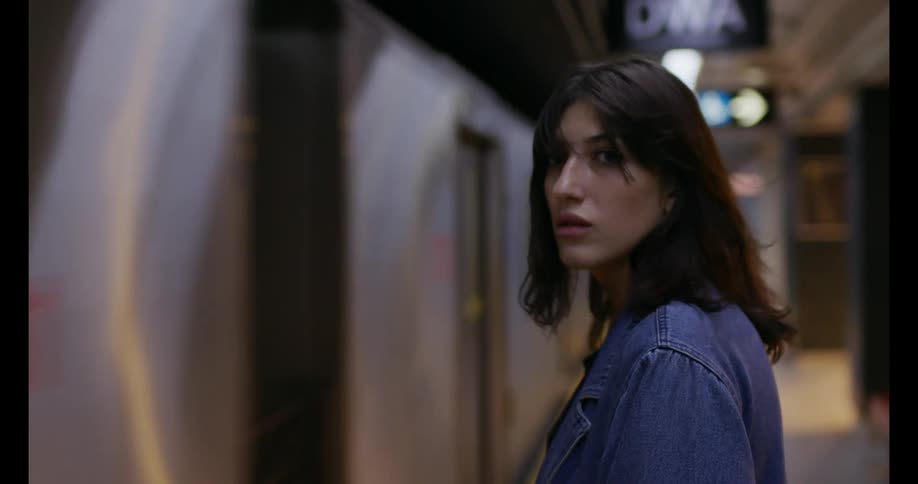 A subway car enters the station, blowing a woman's hair in the wind as she waits.