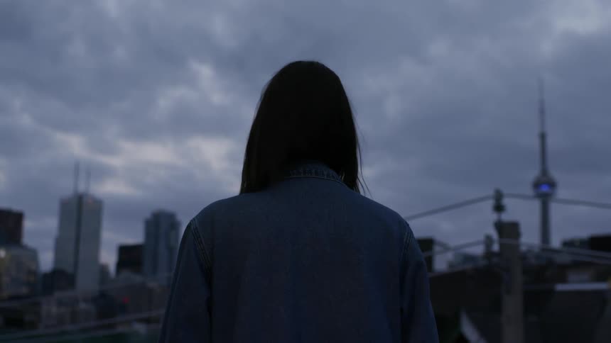 A woman looks over the cloudy city skyline from a rooftop.