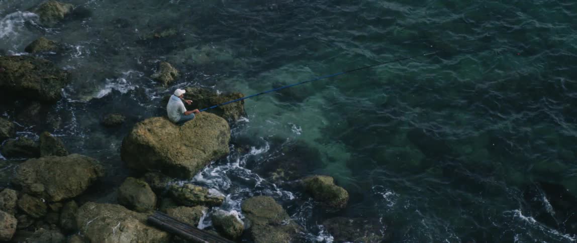 A man fishes from a rock