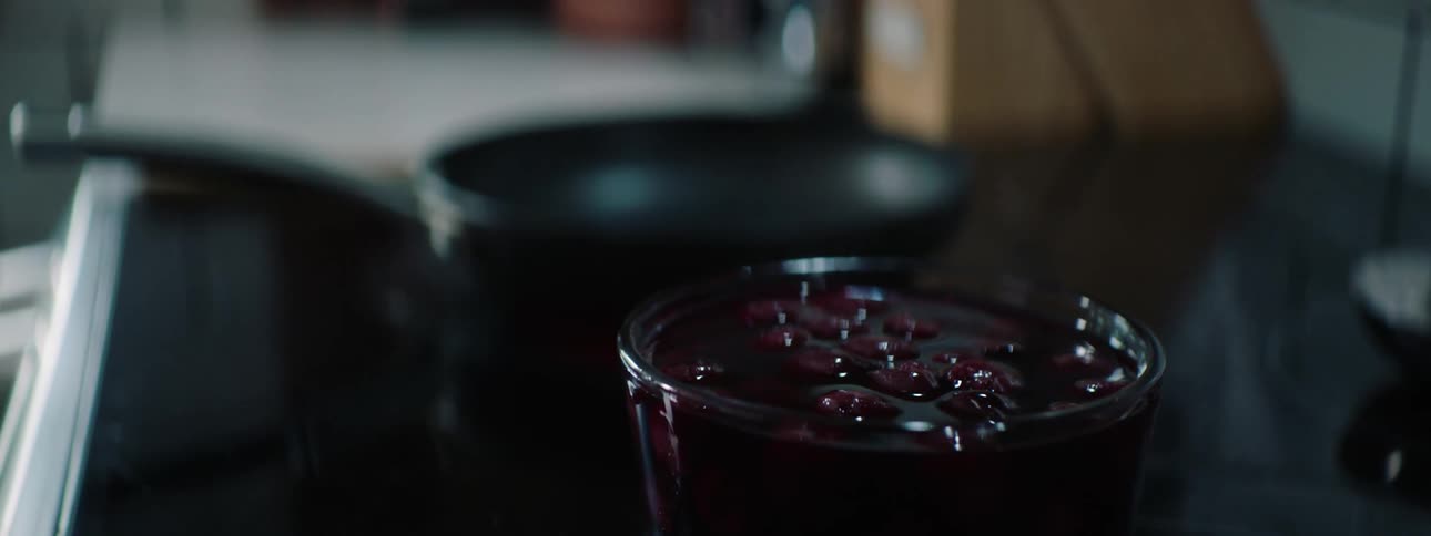A kitchen with a frying pan on a stove next to a jar of cranberry sauce