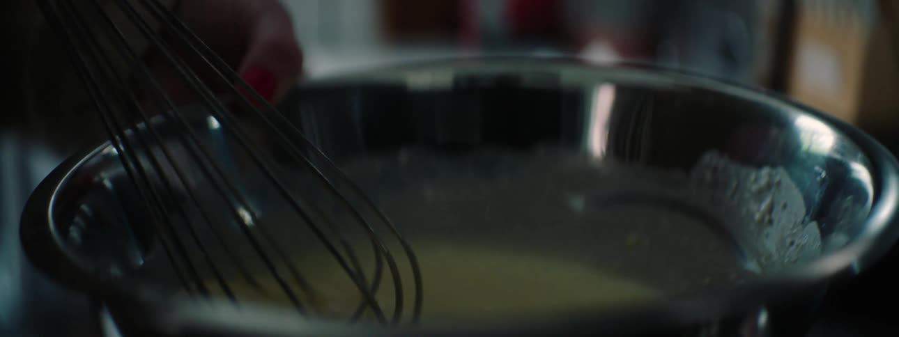 A woman whisks battery in a silver bowl during the day