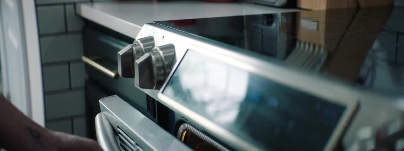 Woman puts tray into oven then sets controls on panel