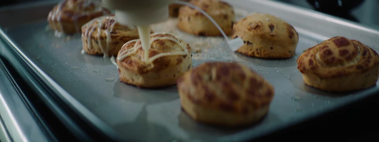 Pastry buns sitting on baking sheet are iced from bottle