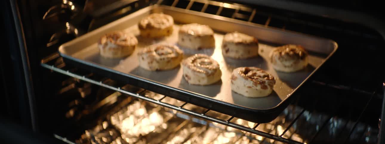 A woman opens her oven and looks at the cinnamon buns baking