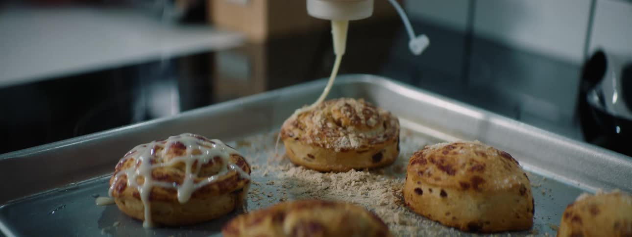 Frosting being placed on pastries on a cooking sheet in the kitchen