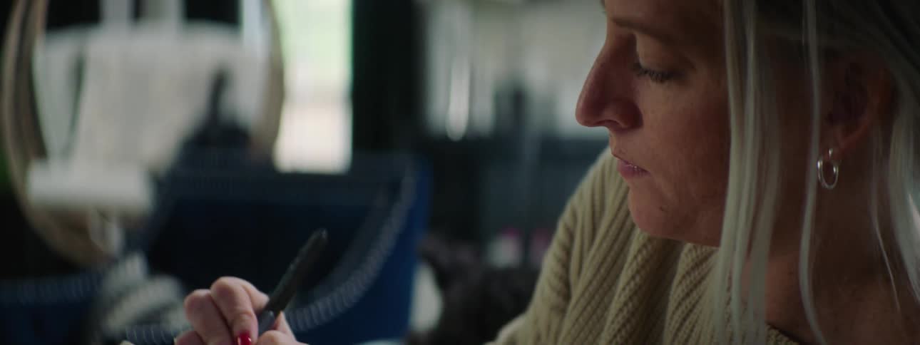 A woman sitting holding a book and writing in it with a pen