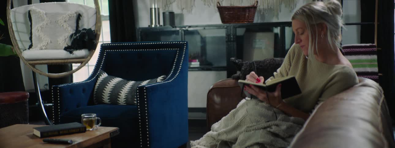 A woman sitting on a couch writing in a book with a pen