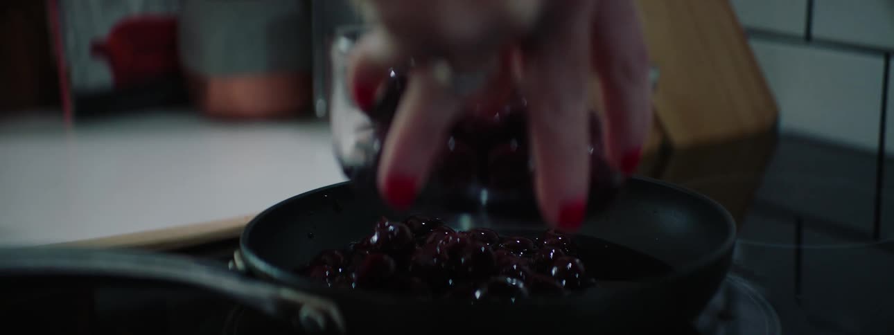 A woman picks up a glass bowl filled with a mix of blueberries and sauce then pours them into a saucepan and begins stirring