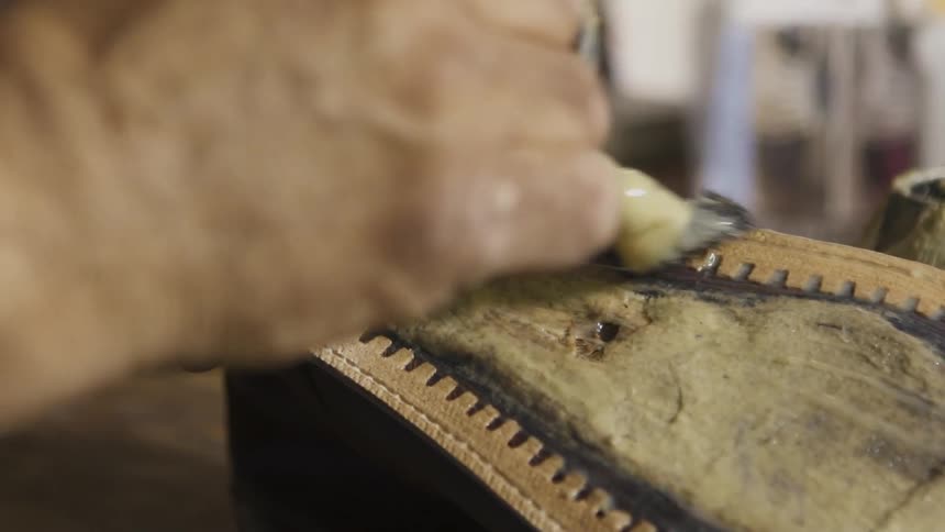 A man spreads glue on the sole of a shoe he is working on