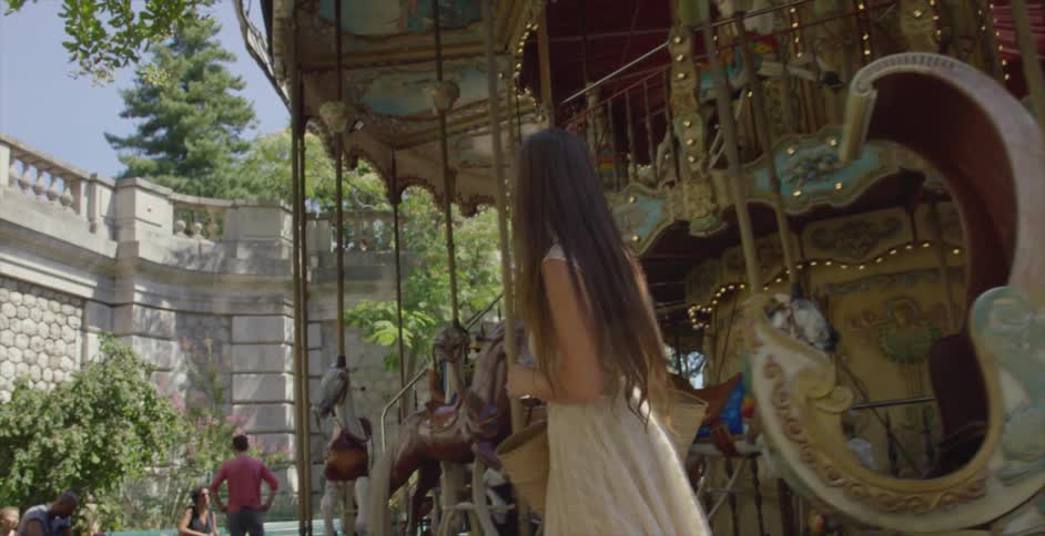 A woman wearing a pale dress walks around a carousel