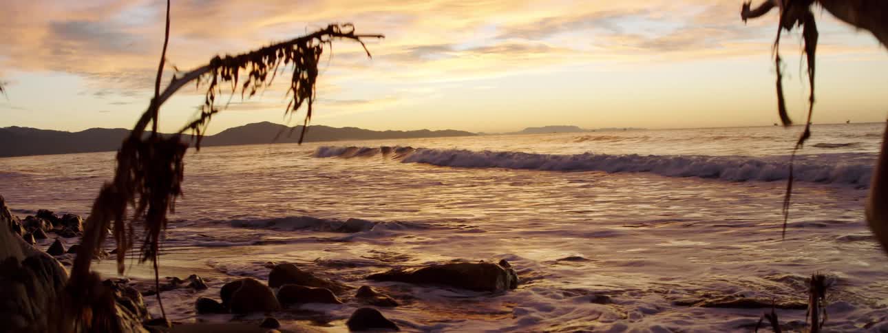 Ocean waves roll into a rocky beach at sunset
