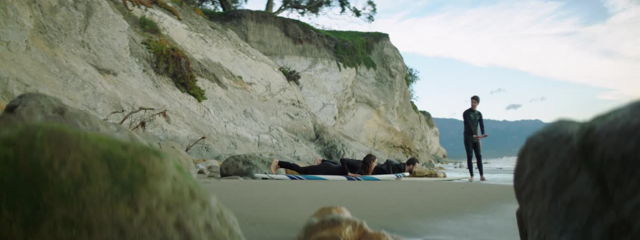 A man instructs a man and woman on surf boards on a beach