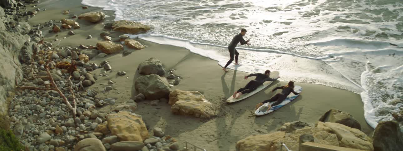 Male instructor gives lessons to a man and woman on how to surf using a surfboard