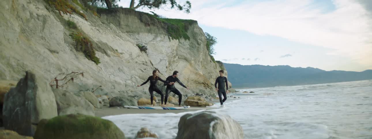 A man and woman on surf boards on the shore listen to a man instructing them