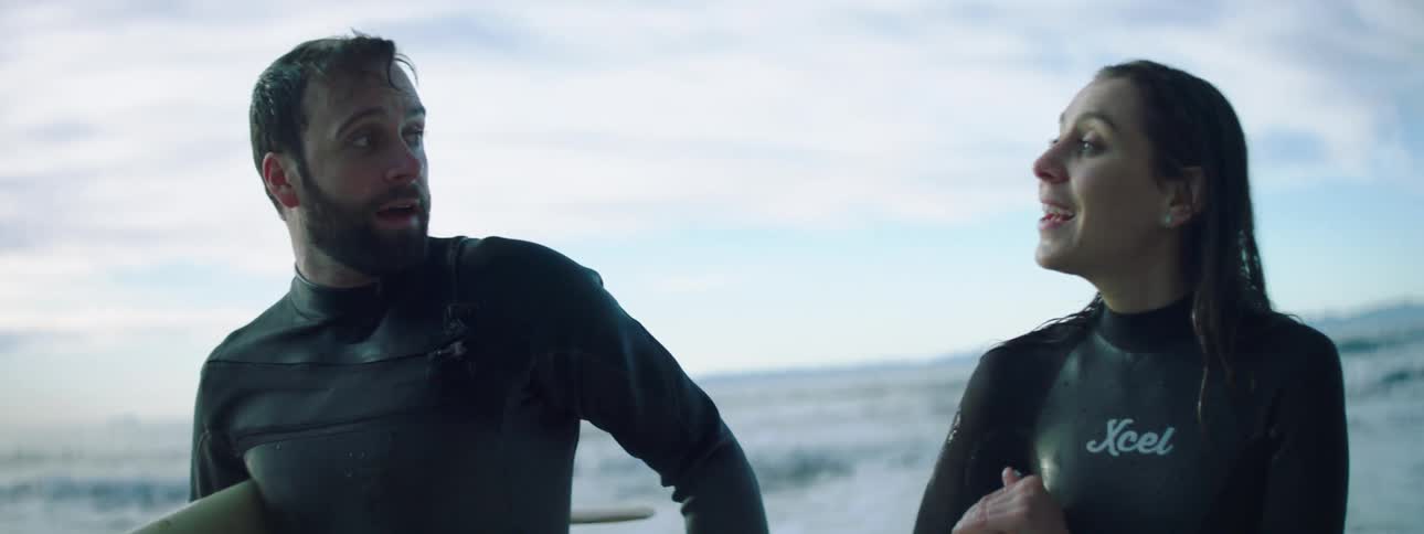 A man and woman chat as they walk out of the ocean with surfboards under their arms