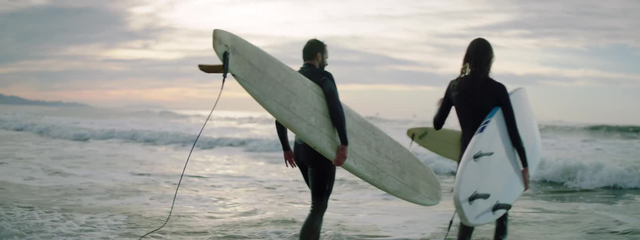 Three people walk in to the water carrying surfboards