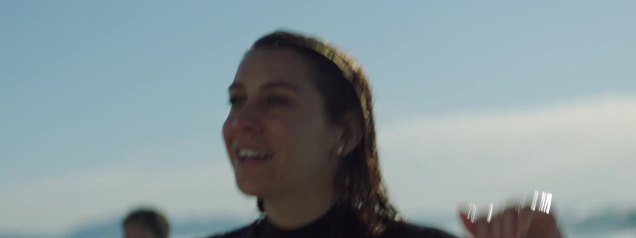 A woman in a wet suit cups her hands before her mouth to call to someone out of frame