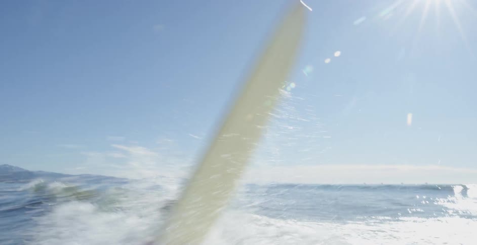 A man laying on a surfboard and swimming then gets hit with a wave