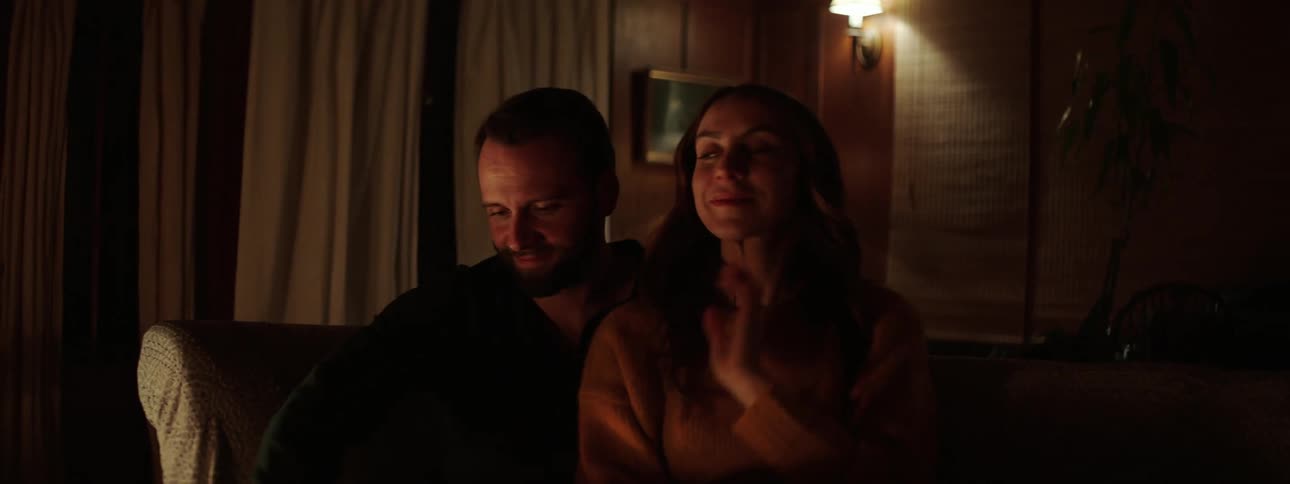 A man and wife sit on the couch put a blanket on and cuddle
