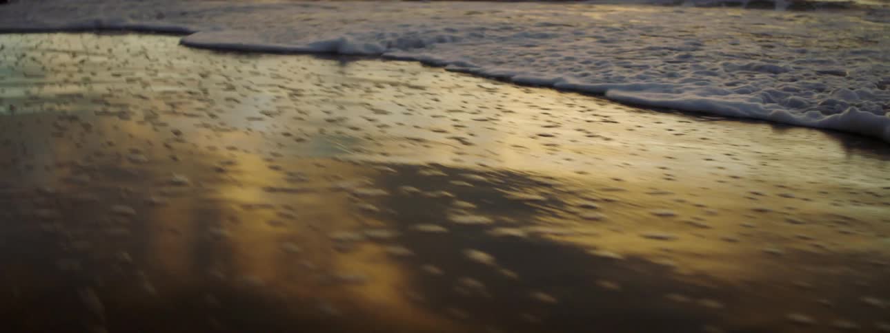 The waves slowly move over the sand at sunrise