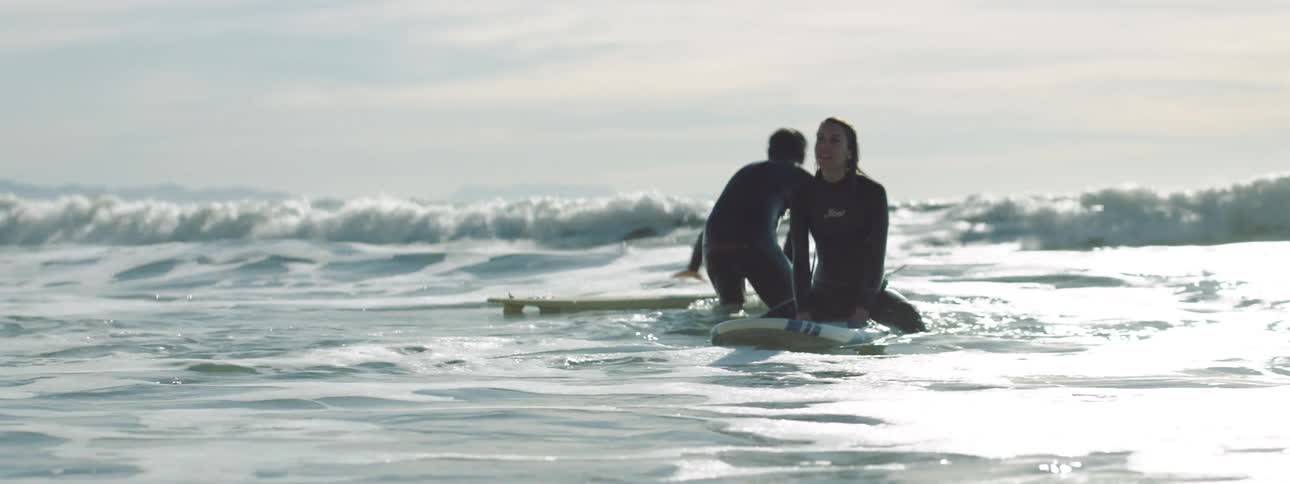 A pair of surfers sit on their boards as they prepare to surf the next sets of waves