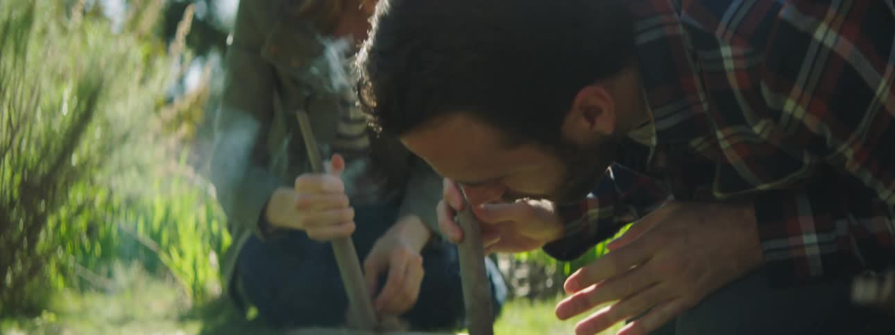 Man and woman each attempt to start a fire by rubbing two sticks together