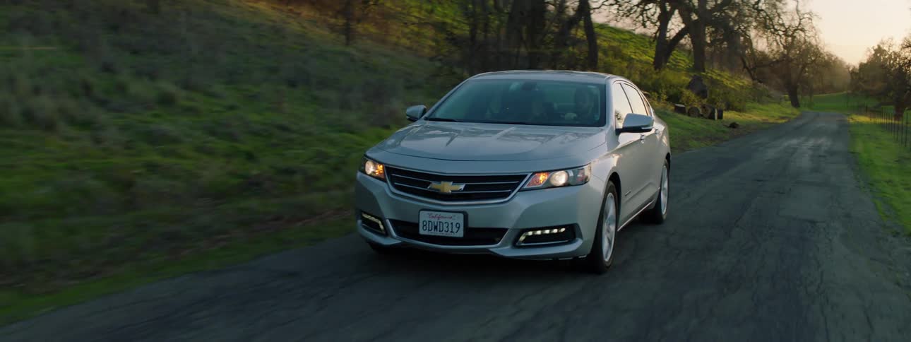 Grey car drives on a country road by a grass hill at sunset