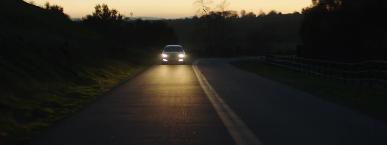 Car having its headlights on drives on a highway at dusk