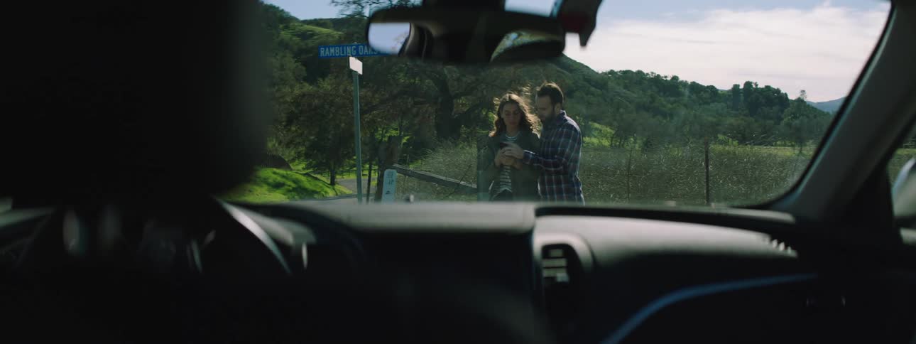 Man and woman stand in front of a vehicle near a field