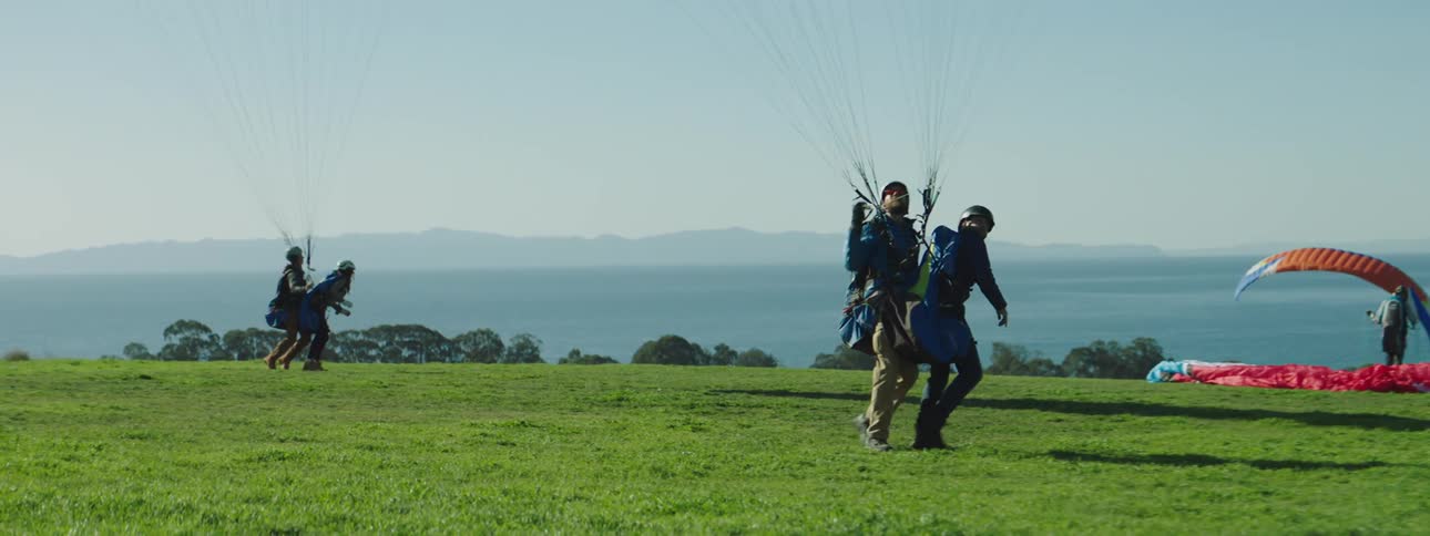 People with helmets and jackets paragliding near the coast with the sky in the background