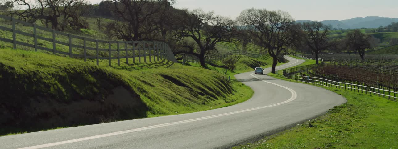 Car drives down a road on a rural farmland area at day