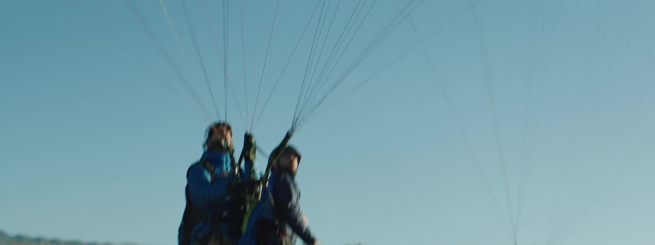 Four people hooked up to parachutes on a grassy field