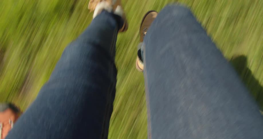 A females legs dangling over the grass as they hang off a truck driving