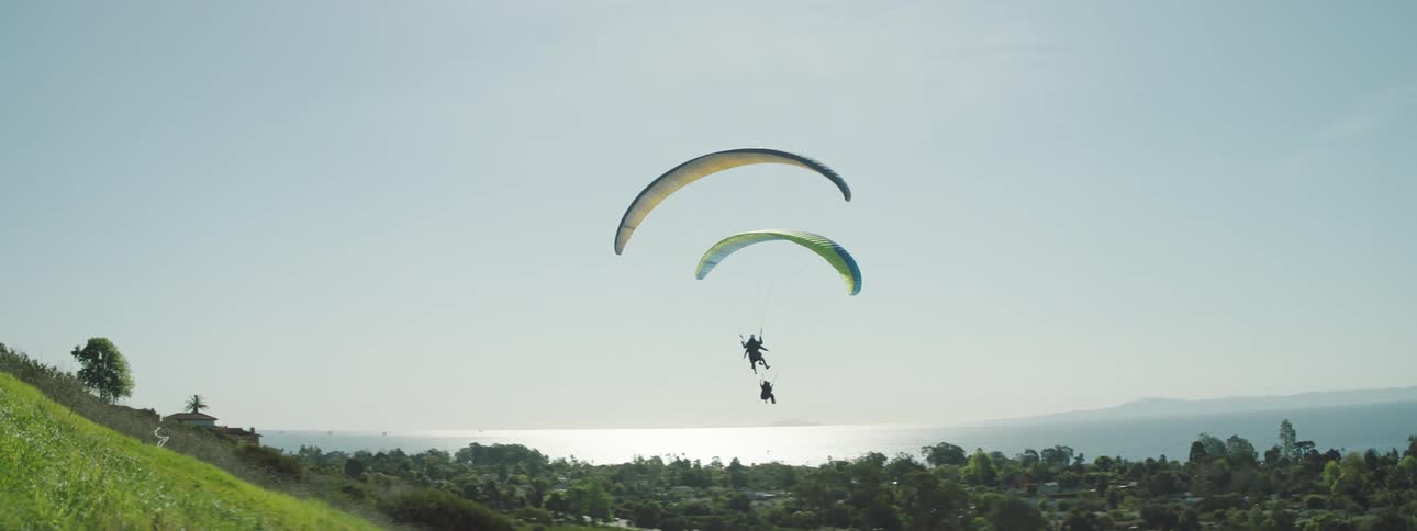 A couple of paragliders floating down a hill near the sea at day