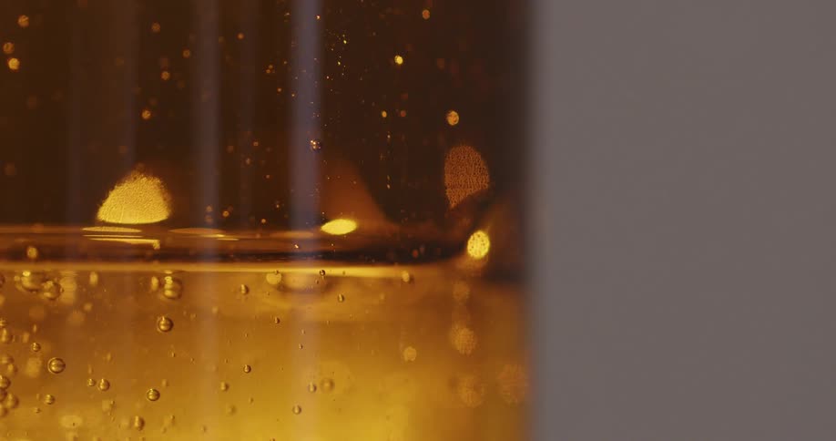 Amber liquid with bubbles in glass container against grey background