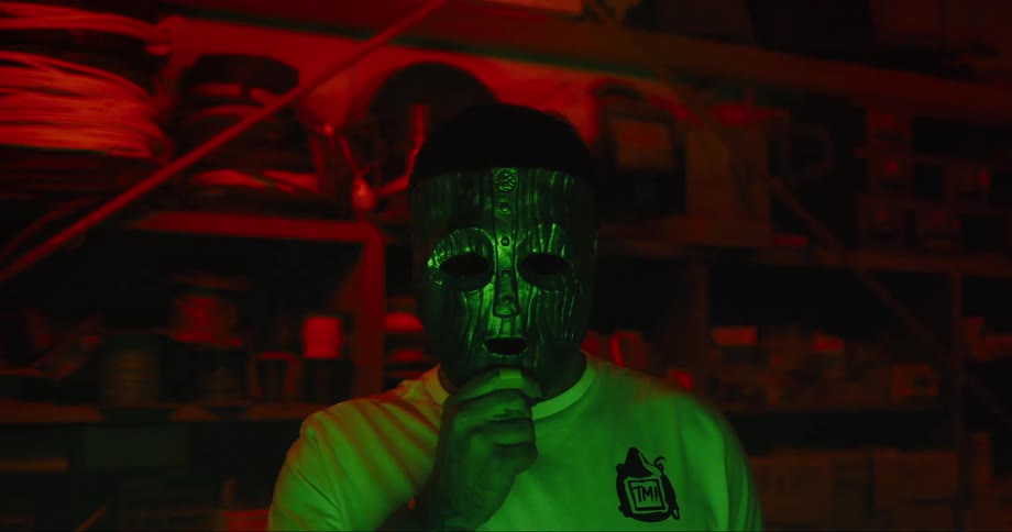 Colored static flashes on the screen as a man puts on a full face carved mask
