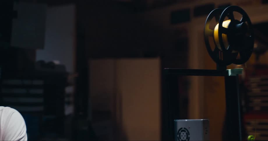 A man sits in a dimly lit room and uses a laptop at a desk