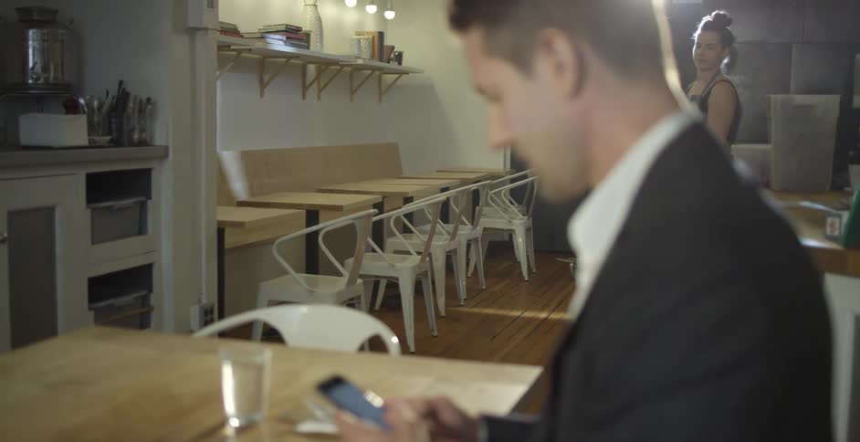 A waitress serves a man using his phone at the table