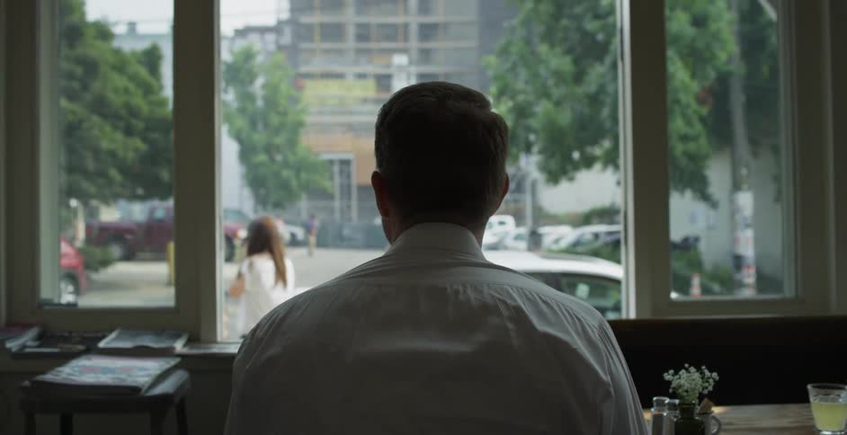 A man watches pedestrians travel along the street through the window of a restuarant in which he is eating