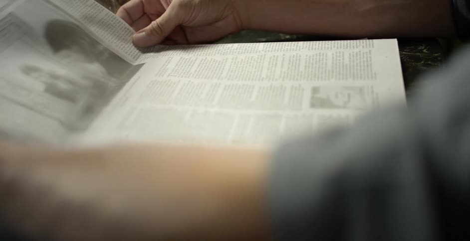 A man reads a newspaper while sitting at a table