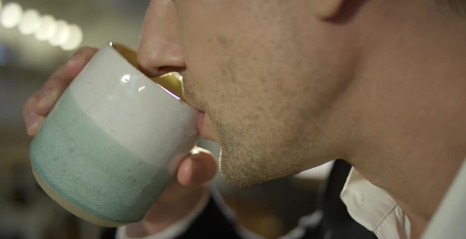 A man takes a hot drink from his mug