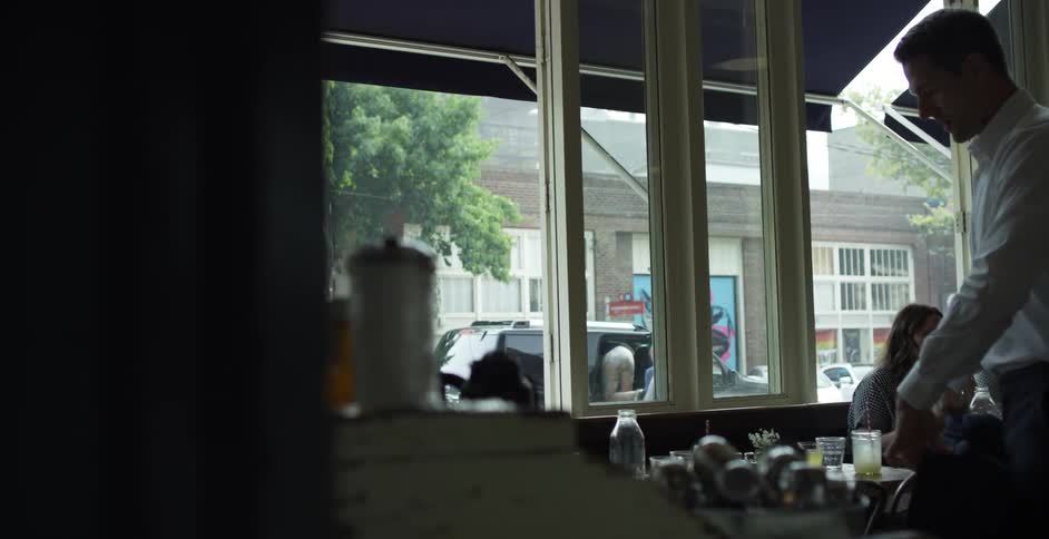 A man in a restaurant taking off his jacket putting it on a chair and sitting down
