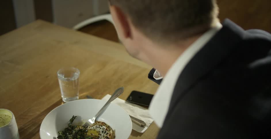 A man in a suit eats breakfast at a dining table