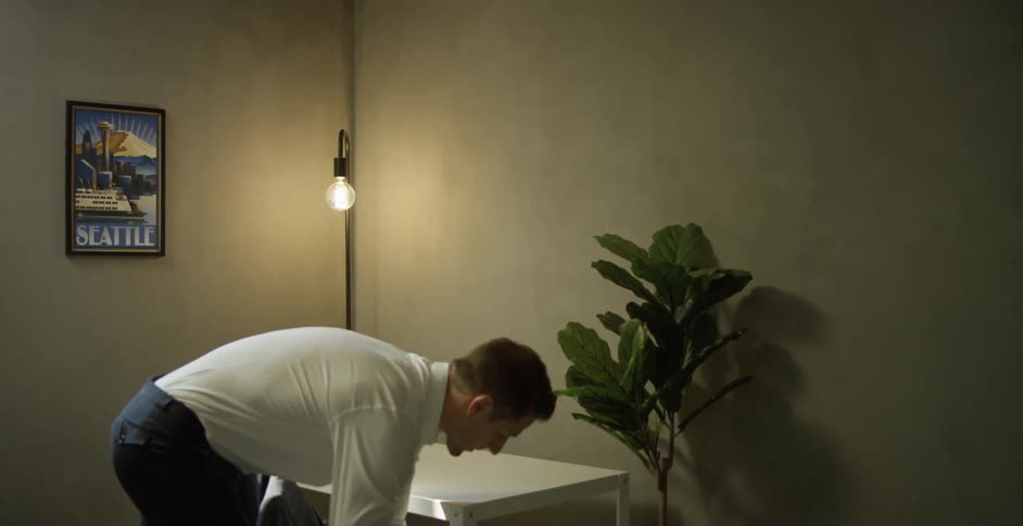 A man standing in front of a table taking a laptop putting it in his bag and taking his jacket and walking