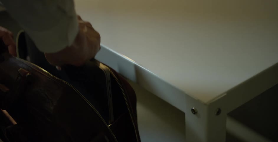 A man closes his apple laptop and places it in a laptop bag before lifting the bag and his jacket and walking away