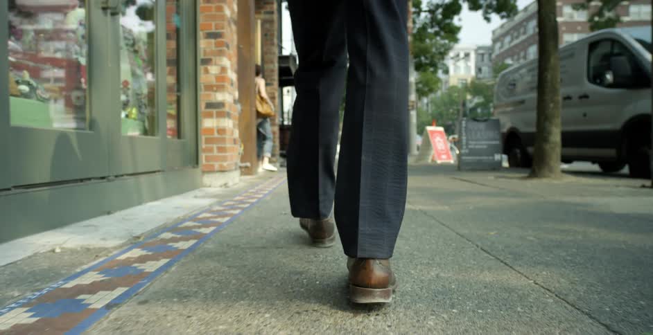 A person walking on a city pavement with trees and buildings in the background