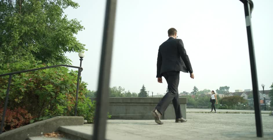 Man climbs up the stairs and walks in the park as a woman walks by