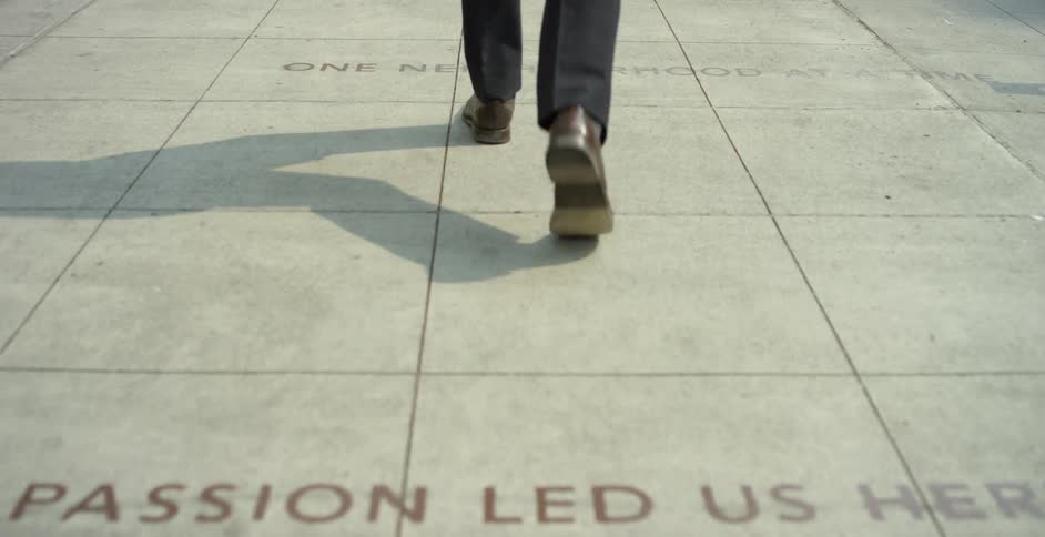 A persons legs walking on the pavement with shoes and pants